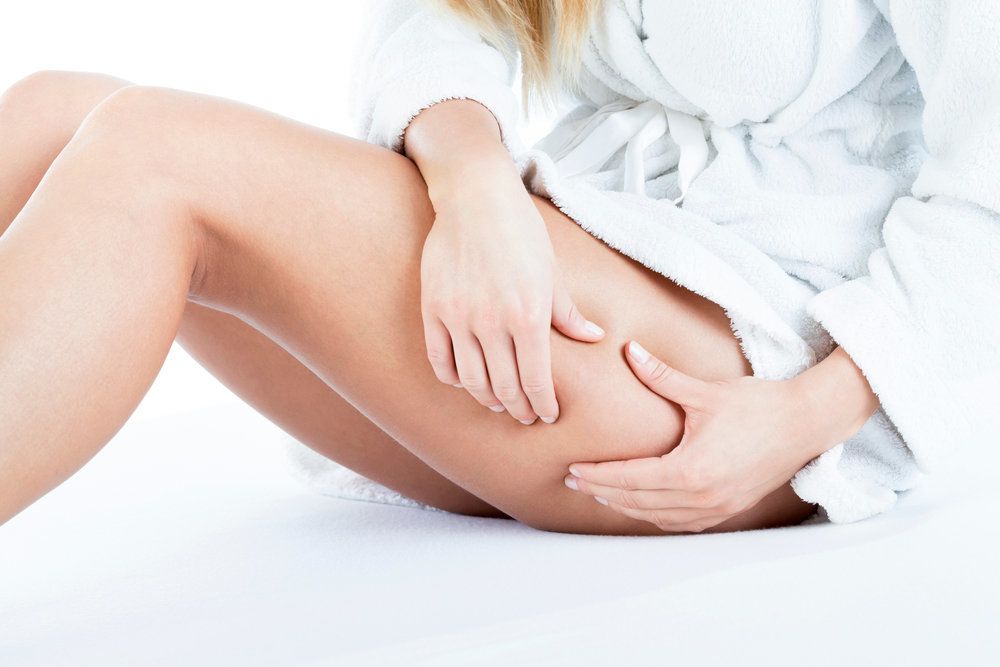 Woman holds thigh area, demonstrating area of thigh lift