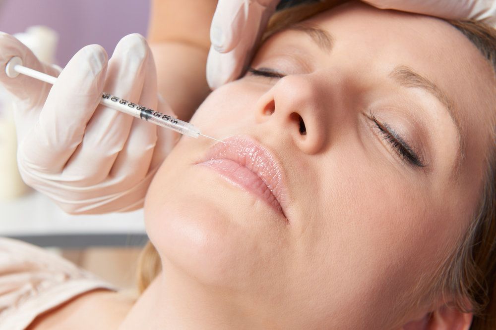 Woman lying down with eyes closed receiving an injection in her face